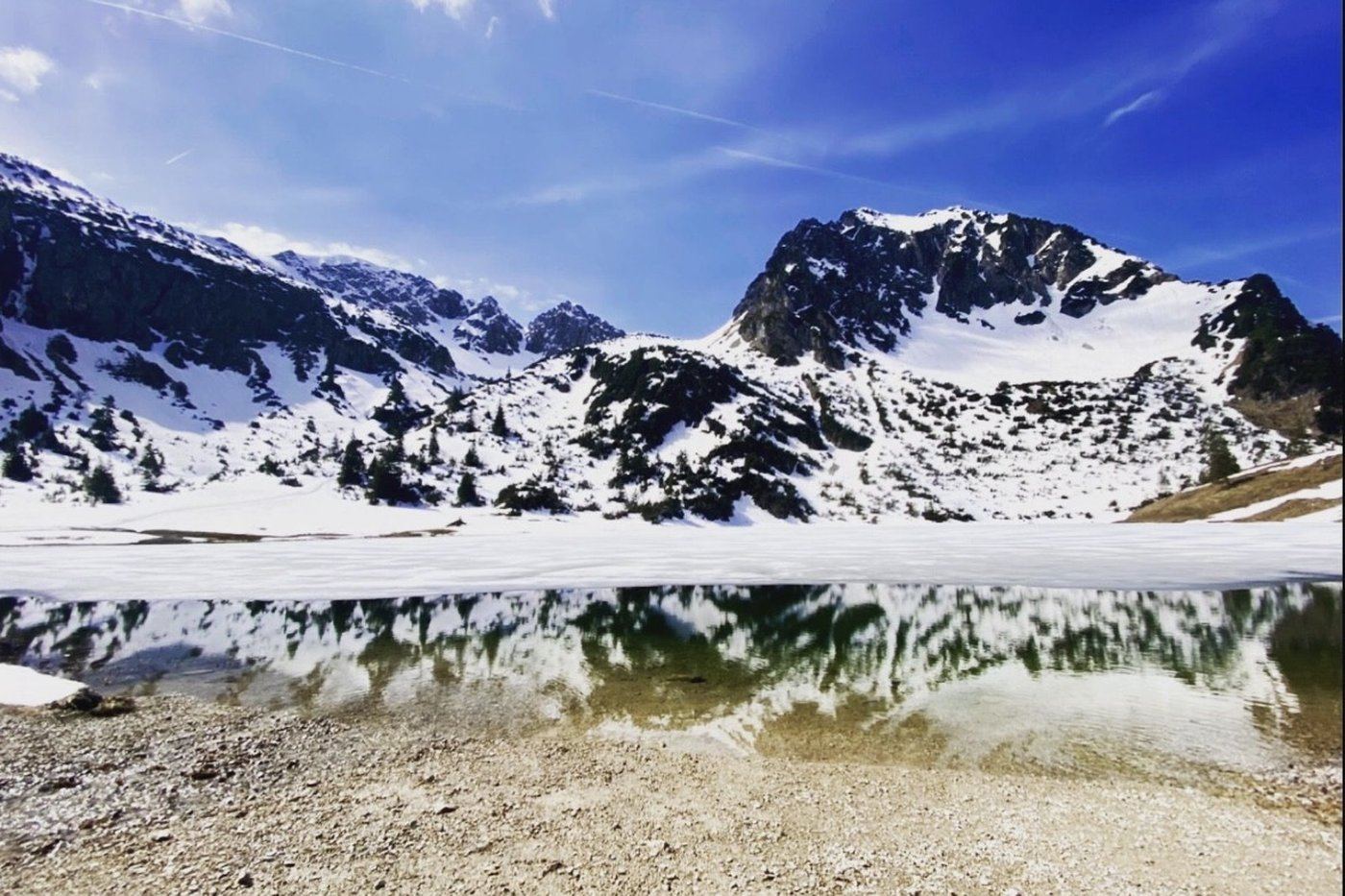 Gaisalpsee im Frühjahr mit halb gefrorener Eisfläche, Spiegelung der Berge im offenen Wasser