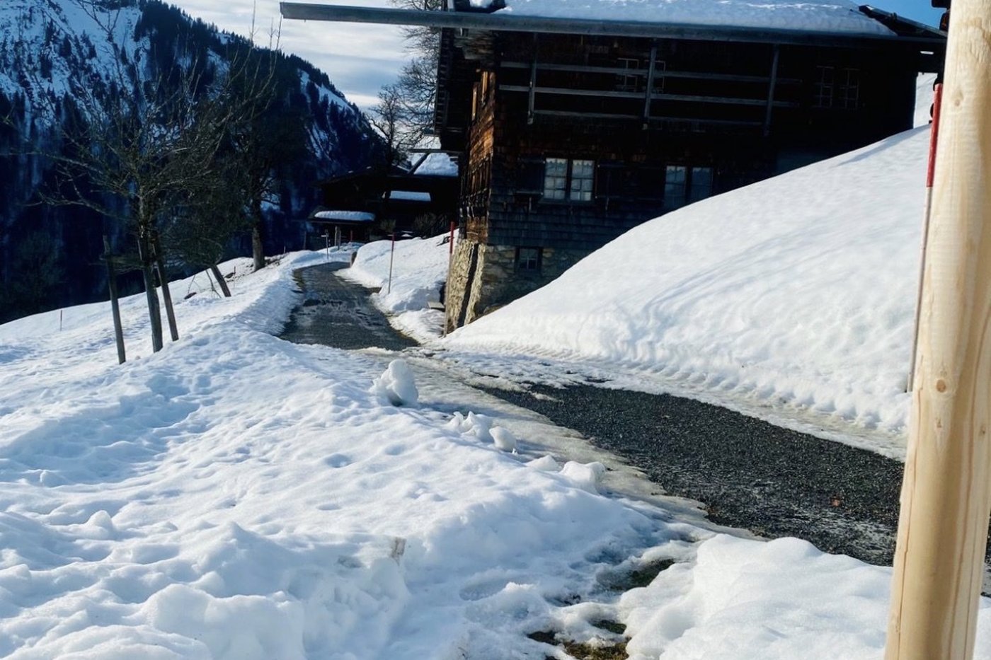 Snow-covered alpine hut with dark wood and a snowy roof, on a trail in the Allgäu