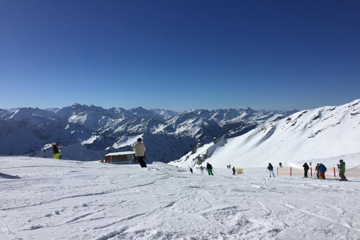 Skiers on a groomed piste at the Nebelhorn, with a wide view of the Allgäu main ridge in the background, clear blue sky