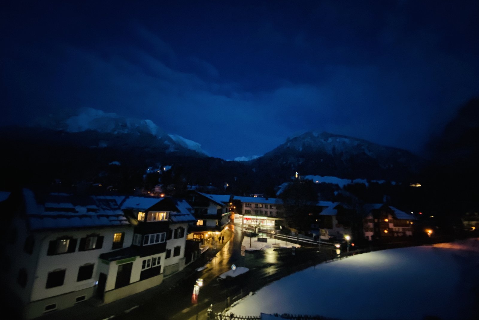 Nächtliches Oberstdorf vom Fenster aus, Straßenlampen spiegeln sich im nassen Pflaster, Berge dunkel im Hintergrund