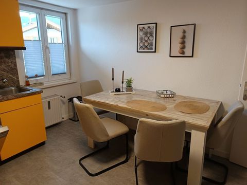 Esstisch für vier mit gelb-oranger Küchenzeile im Hintergrund.