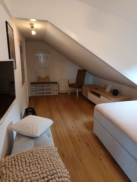 Zweites Schlafzimmer mit schräger Decke, Boxspringbett rechts, Sitzbank links, warmer Holzboden.