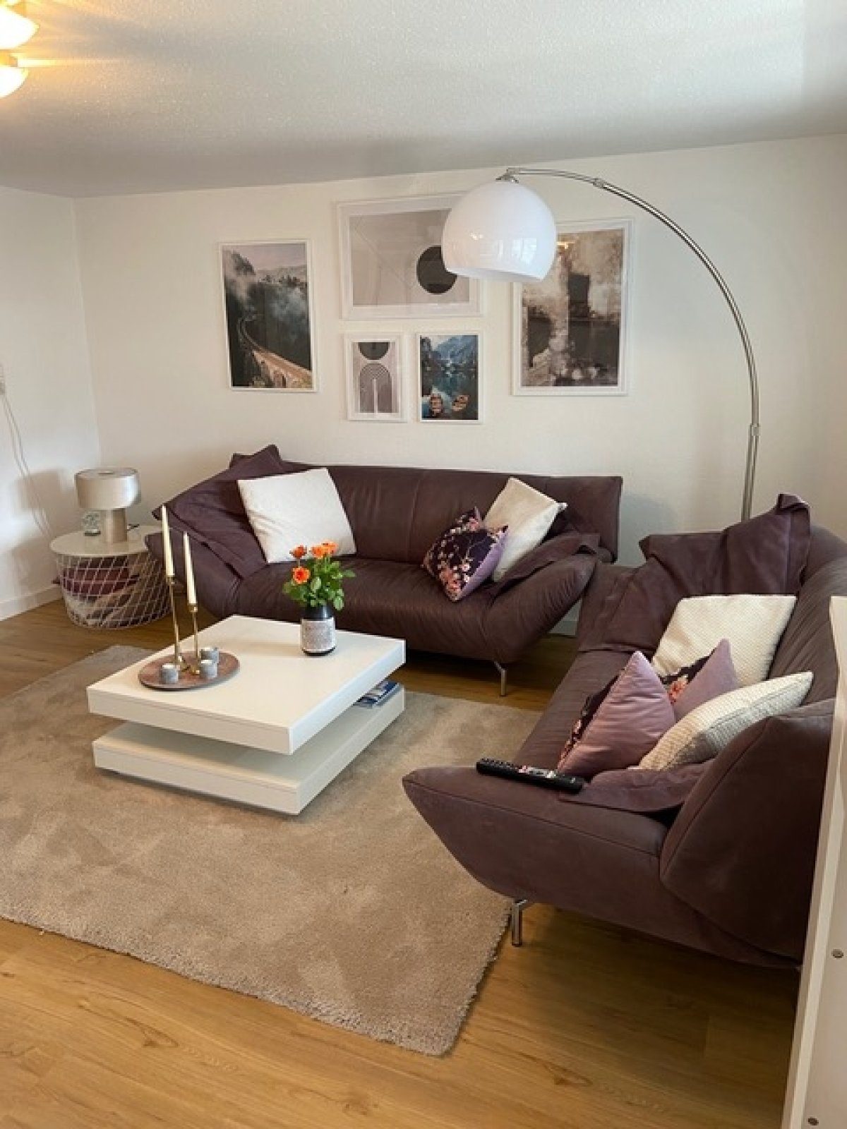 Wohnzimmer der Ferienwohnung Catarina mit zwei dunklen Ledersofas, Bogenlampe und Bildergalerie an der Wand.