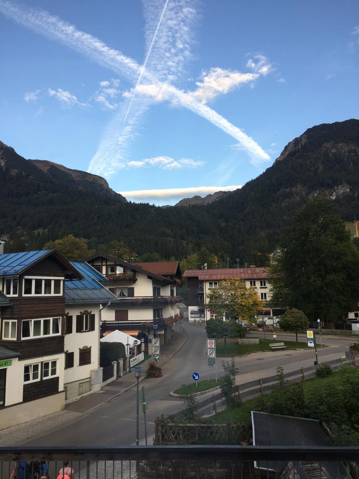 Sommerabend mit X-förmigen Kondensstreifen über den Bergen, Blick aus dem Hannes-Mansardenfenster über die Häuser von Oberstdorf