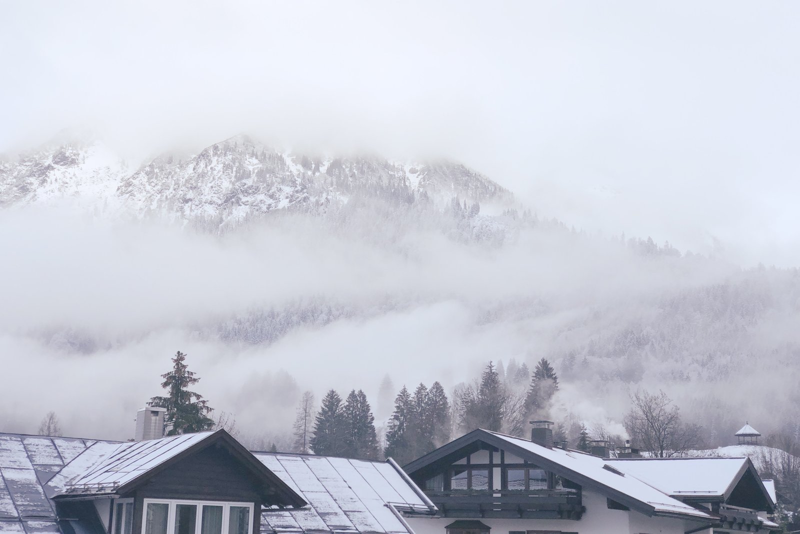 Verschneiter Bergkamm halb in Wolken, Tal in Nebelschwaden, Allgäuer Holzhäuser im Vordergrund