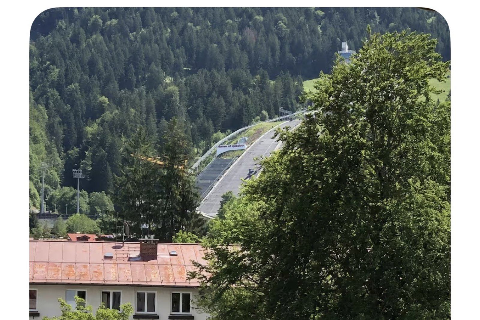 Heini-Klopfer-Skiflugschanze im Sommer hinter Bäumen und Häusern, Blick aus dem Fenster der Wohnung