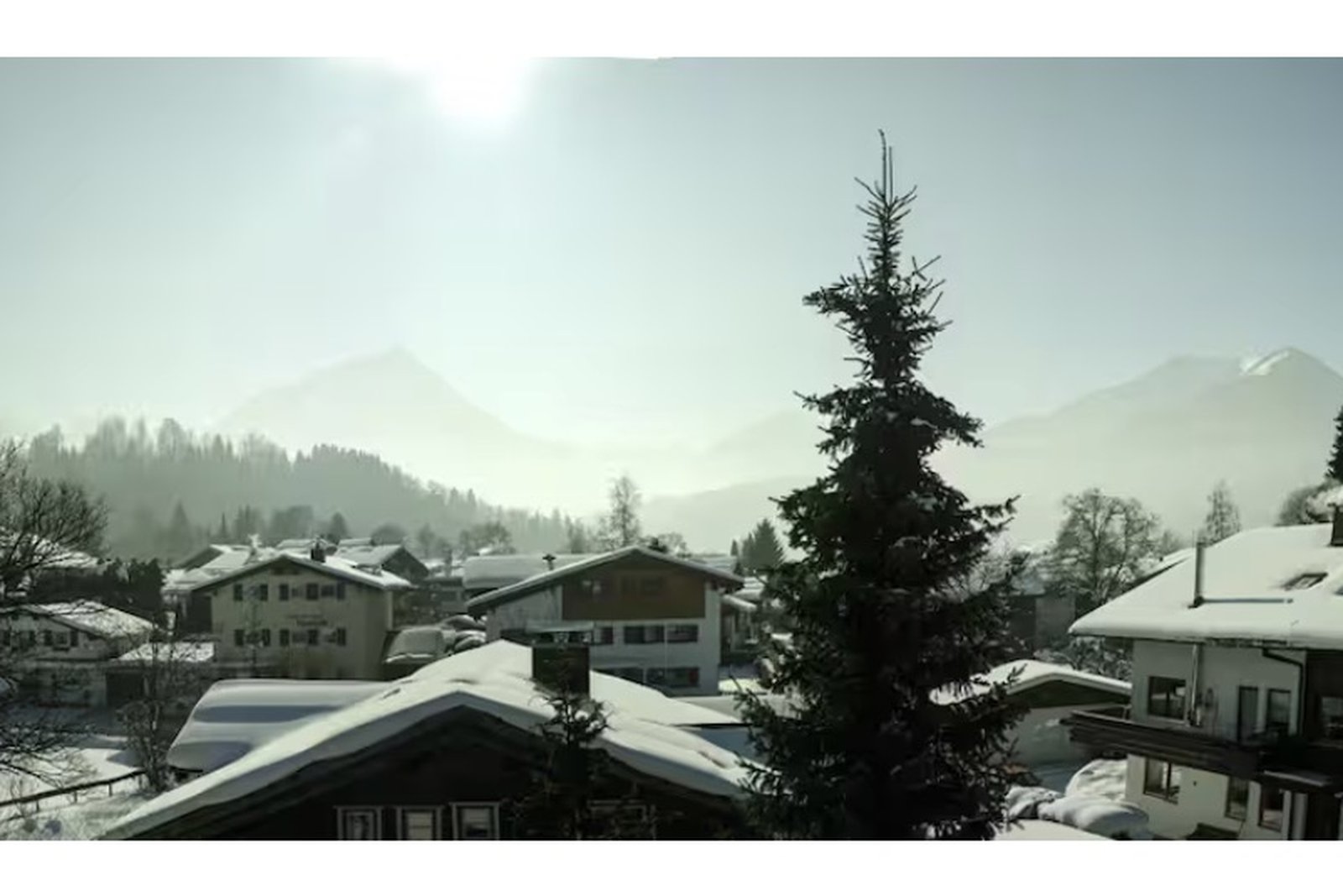 Wintermorgen mit Sonne im Gegenlicht über verschneiten Dächern in Oberstdorf, Allgäuer Berge im weichen Dunst