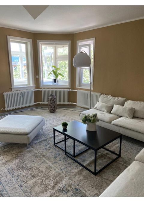 Wohnzimmer-Erker mit drei großen Fenstern, weißem Sofa und Couchtisch im Vormittagslicht.